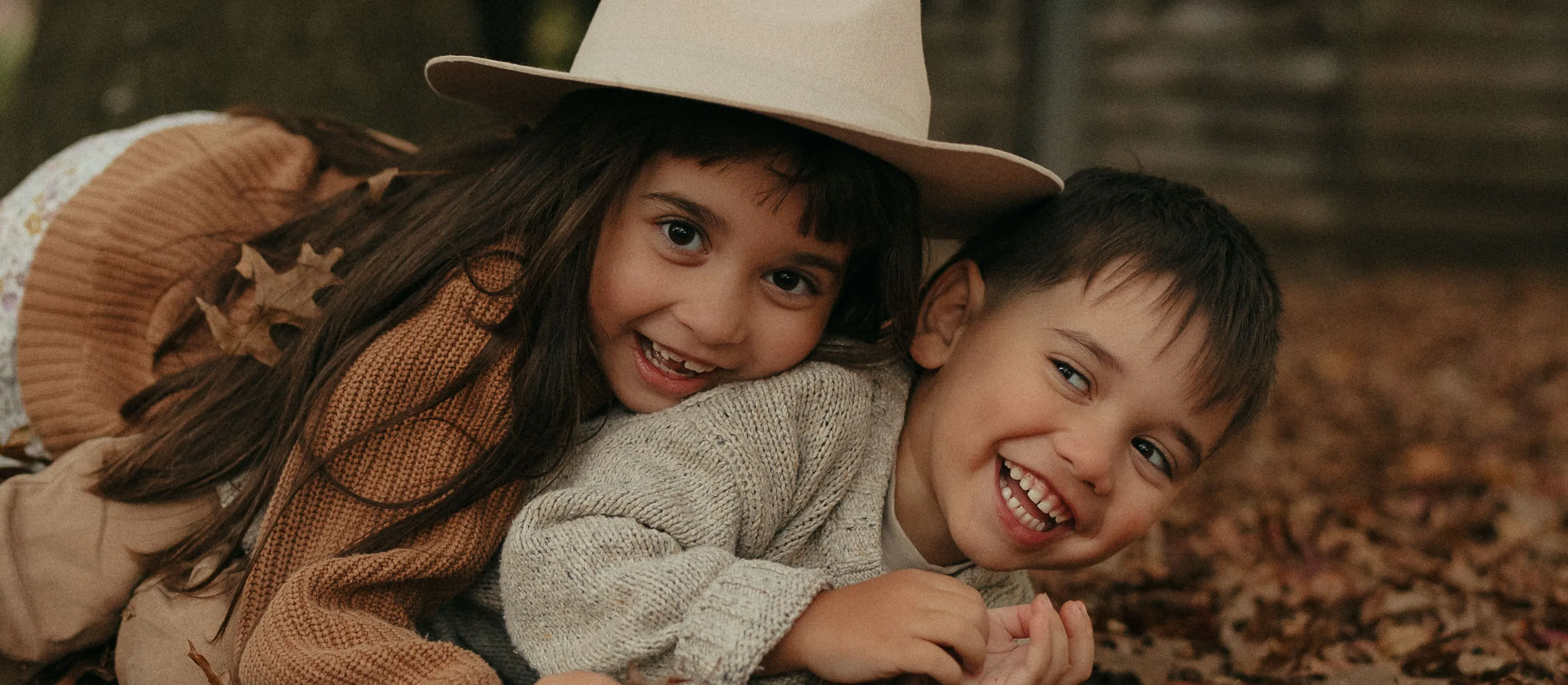 Two kids lying in autumn leaves, grinning at the camera