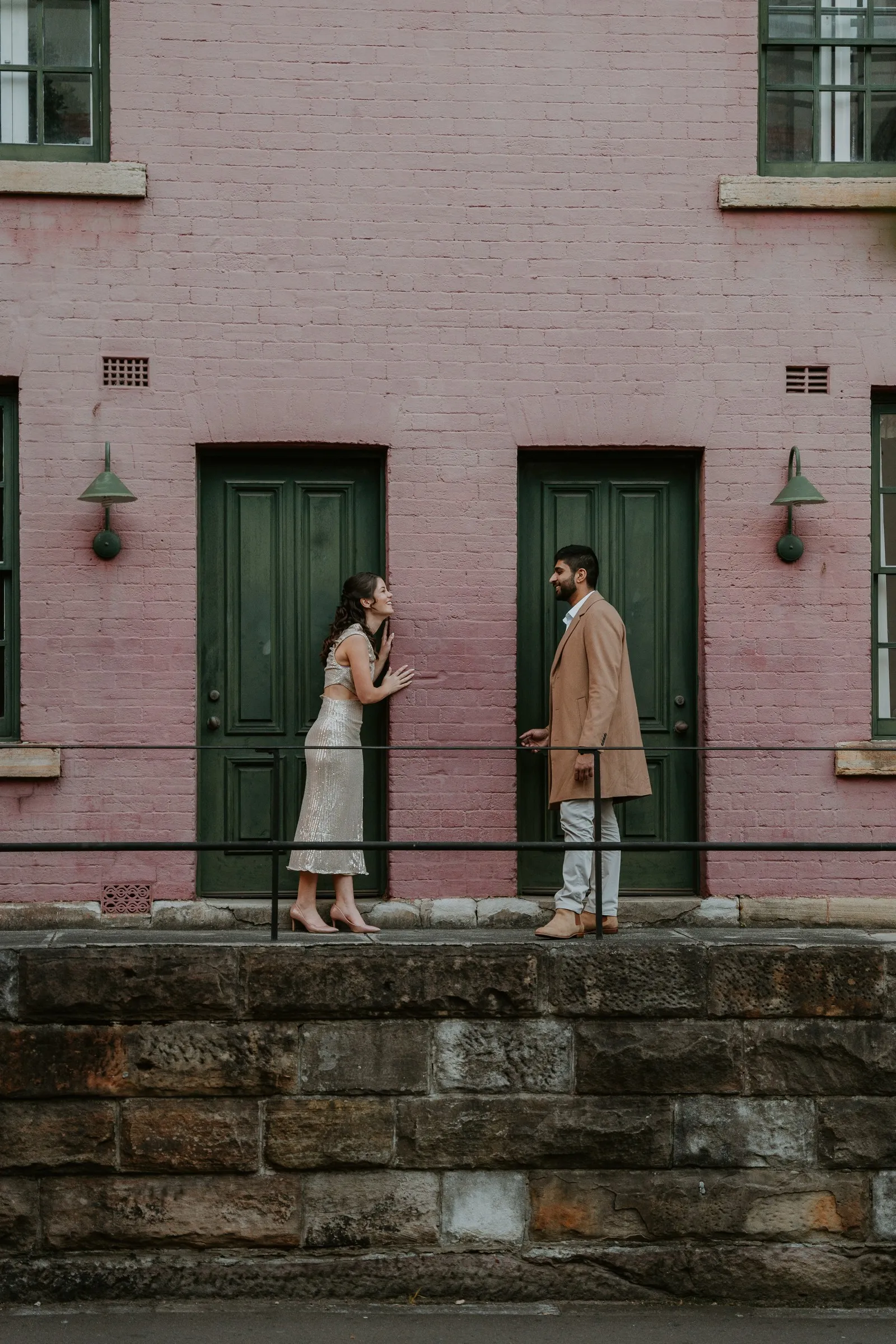 A couple facing each other outside the green door of a pink heritage building