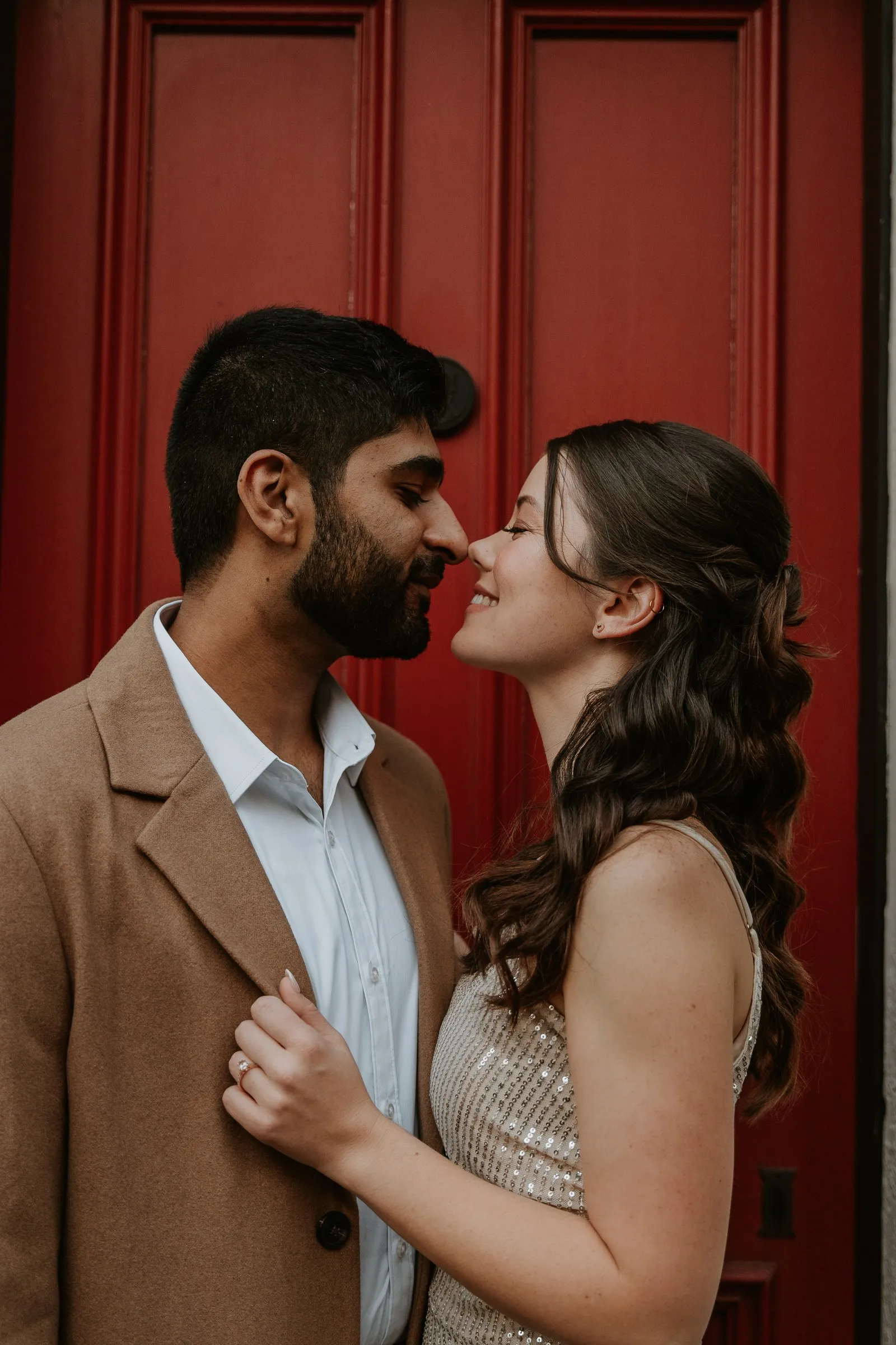 A couple leaning in for a kiss in front of a red door