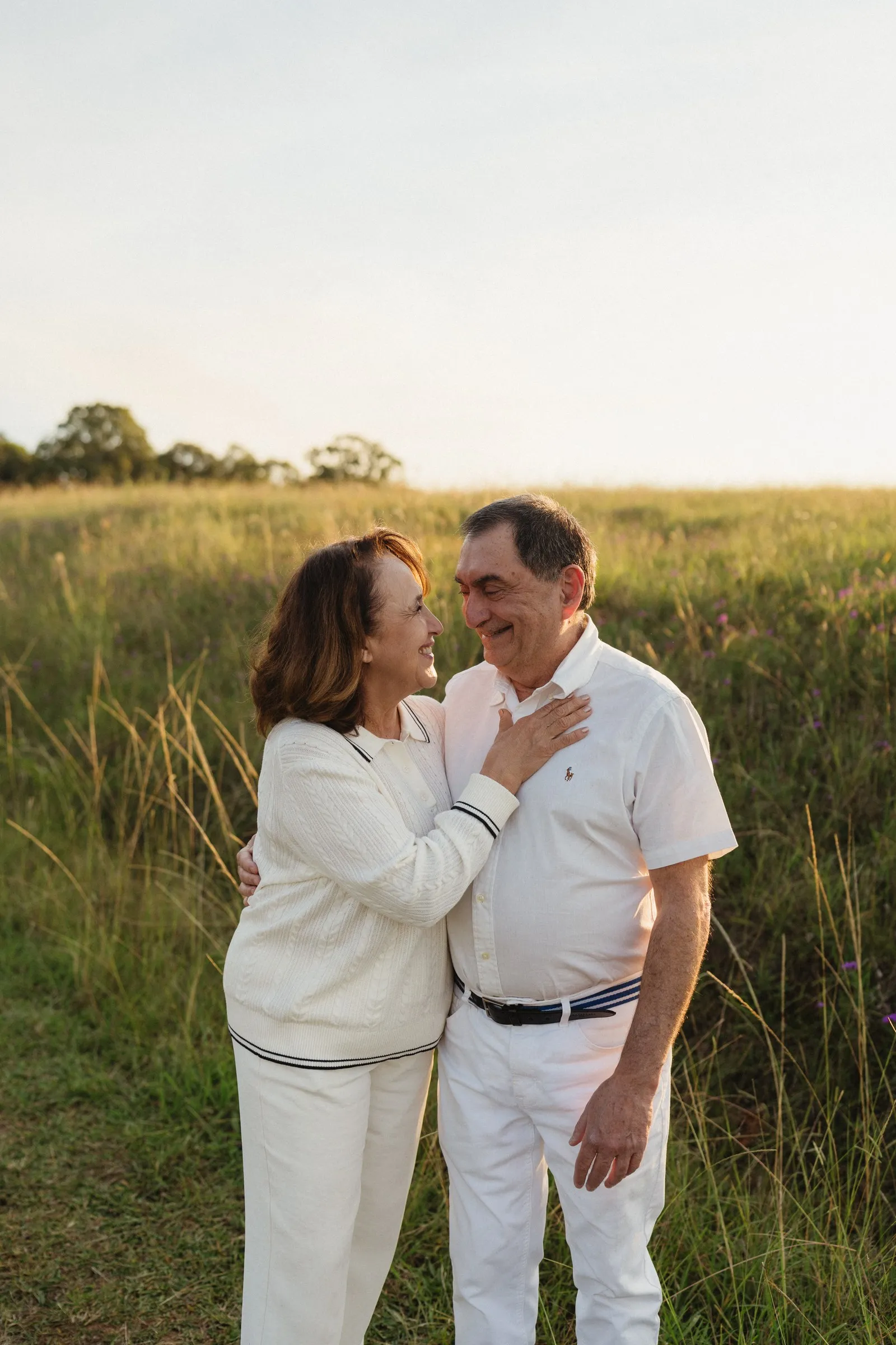 An older couple embracing and smiling at each other in long grass