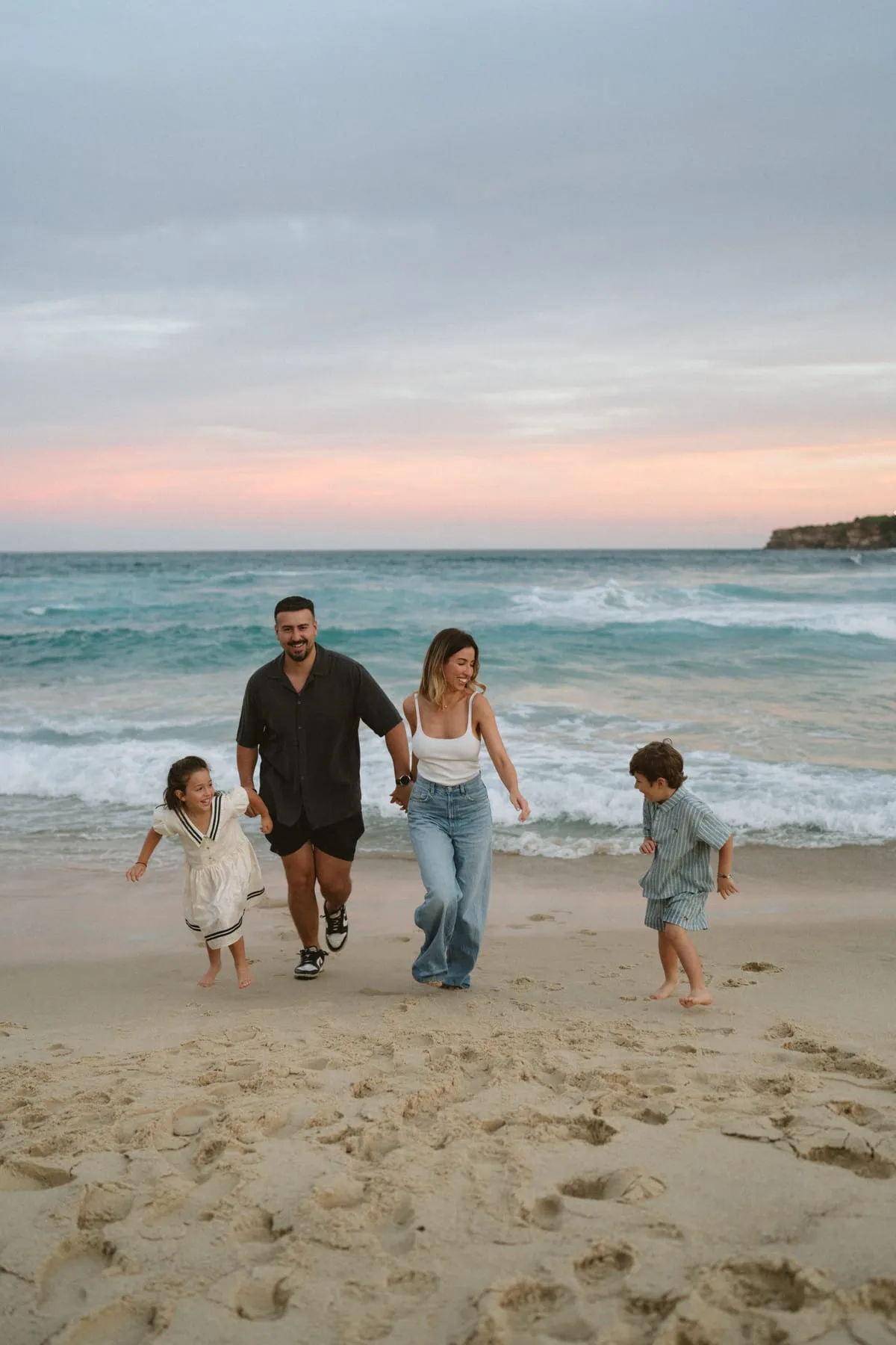 A family walking along the beach under a pink sky