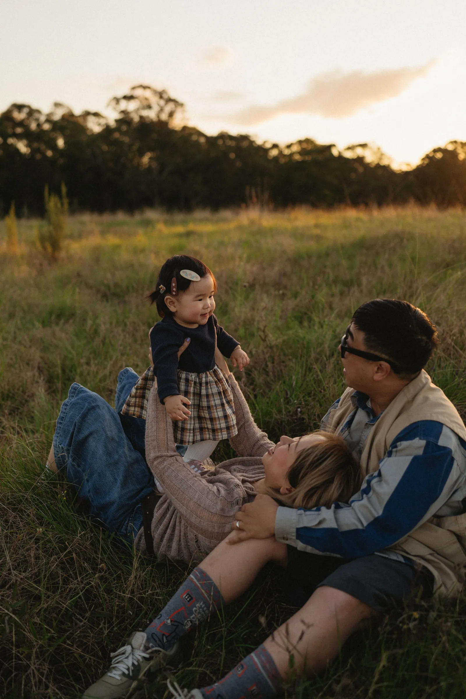 Parents playing with their baby in long grass at golden hour