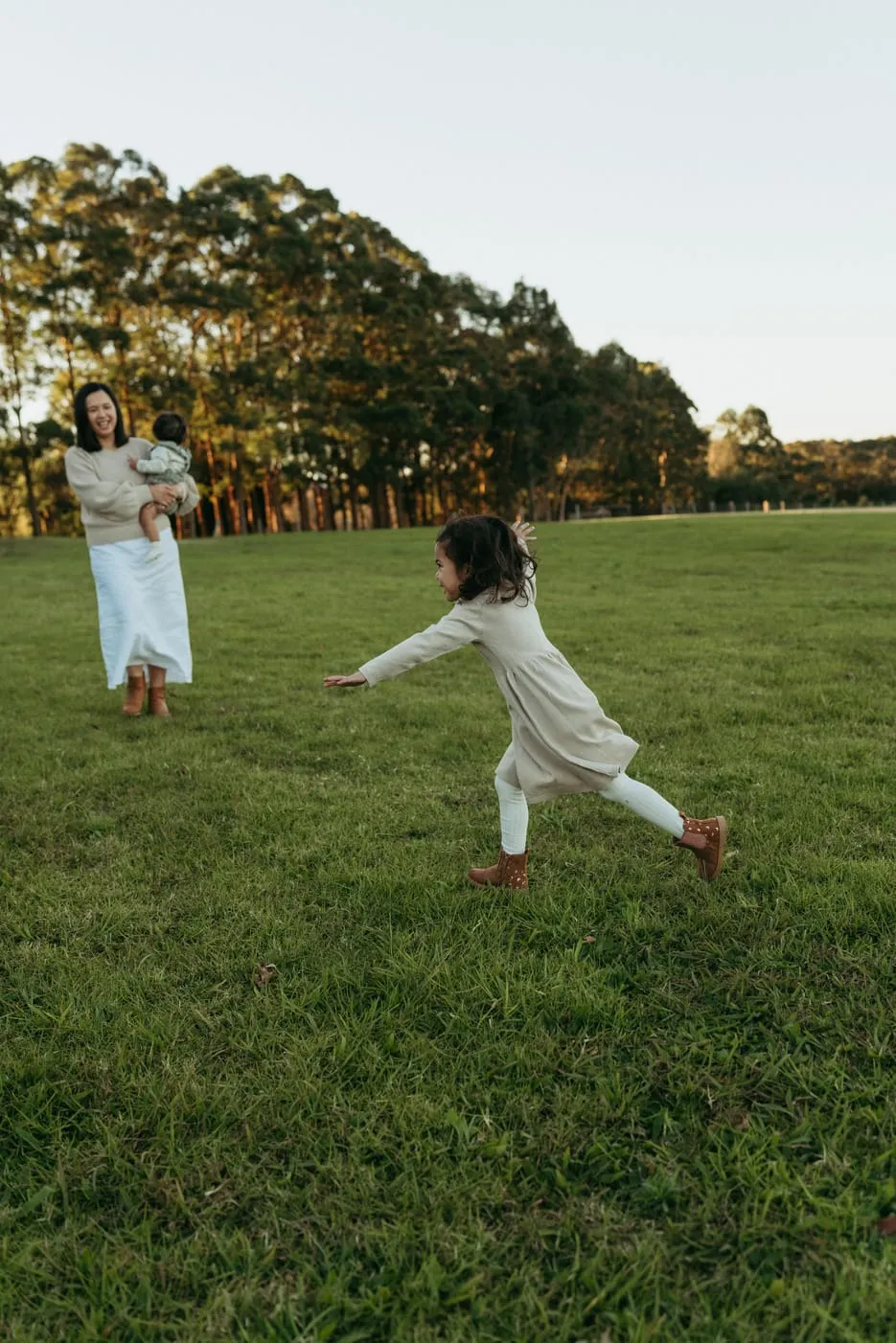 A mum and daughter running across a green park at sunset
