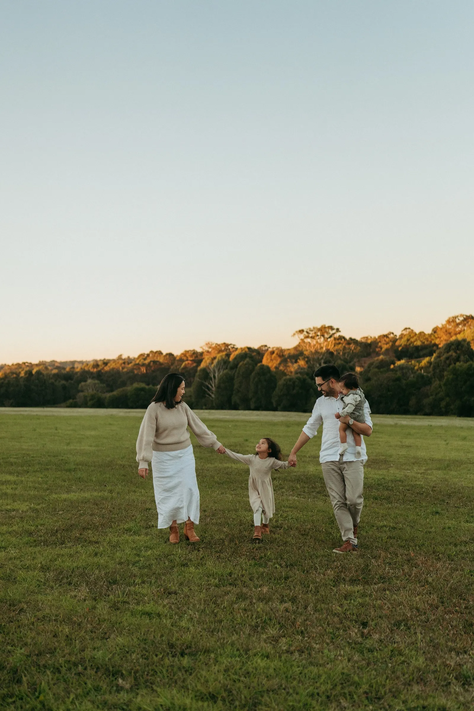 Parents walking hand in hand with their daughter across a field at sunset