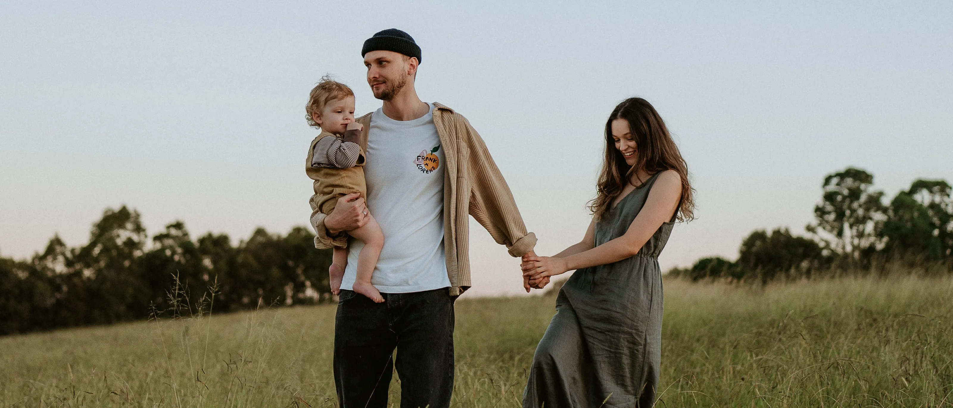 A family standing together in a wide green meadow at dusk