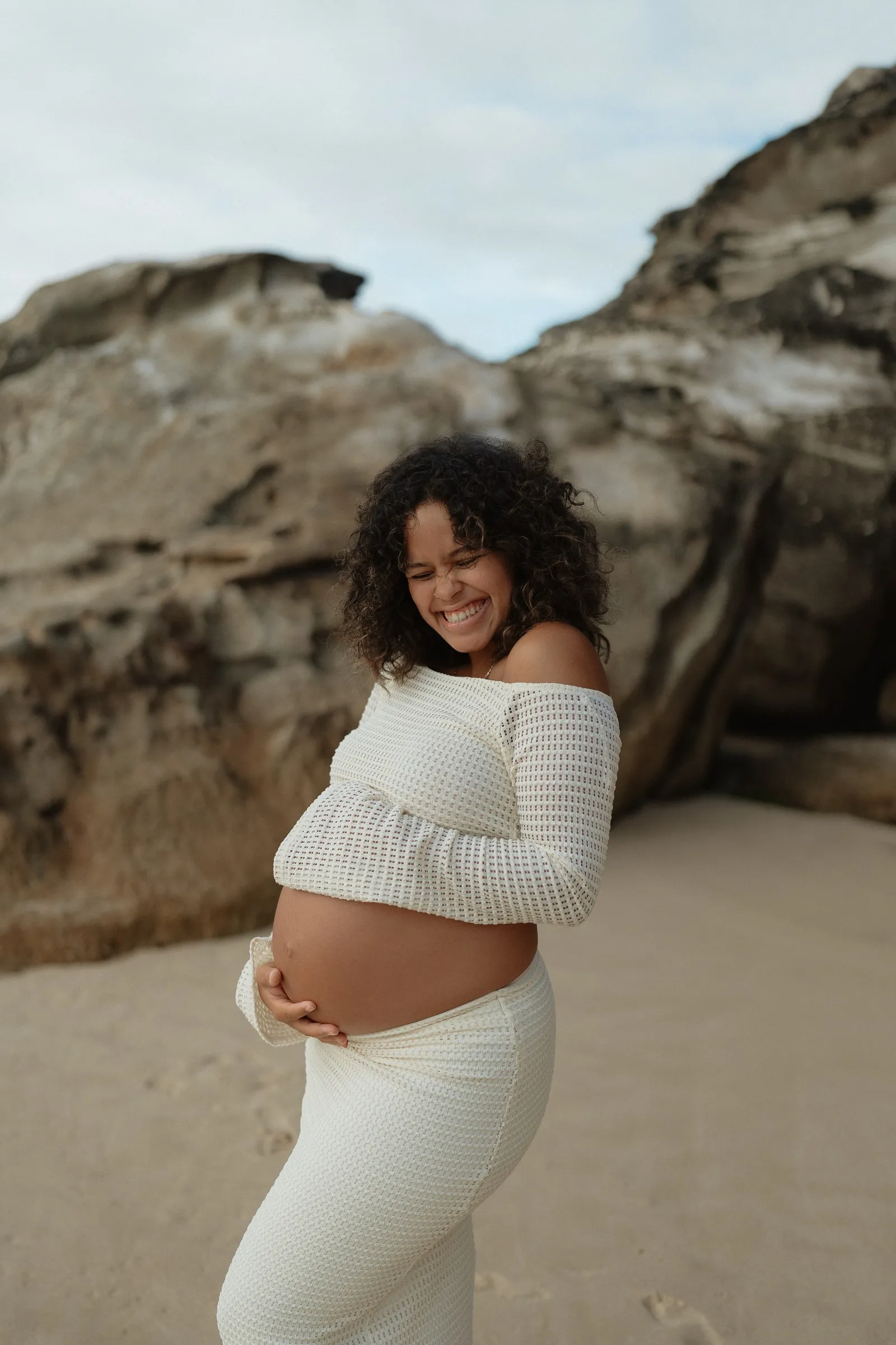 An expecting mum looking down at her bump on the beach