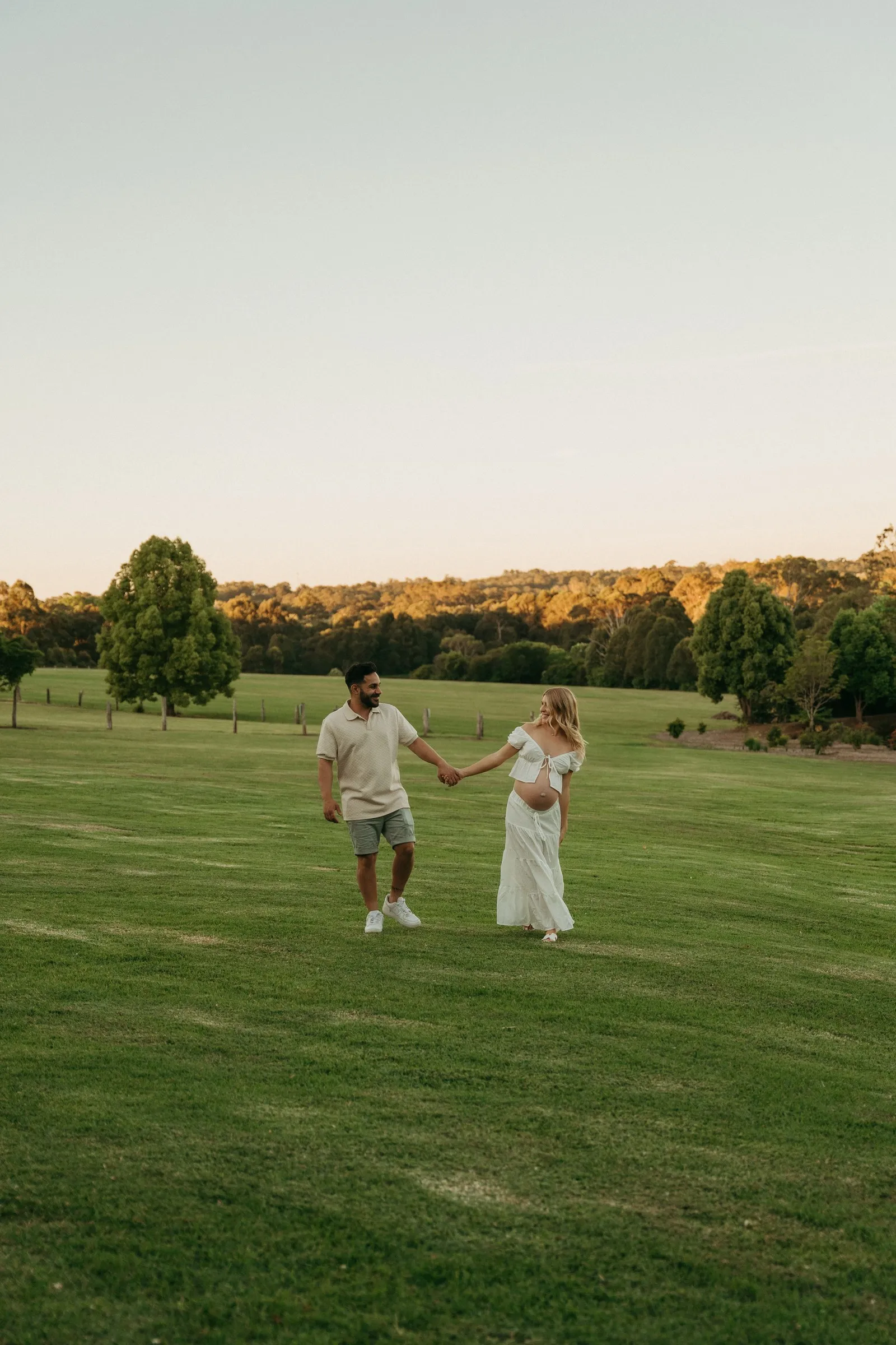 An expecting mum and dad walking hand in hand with their little boy across a field