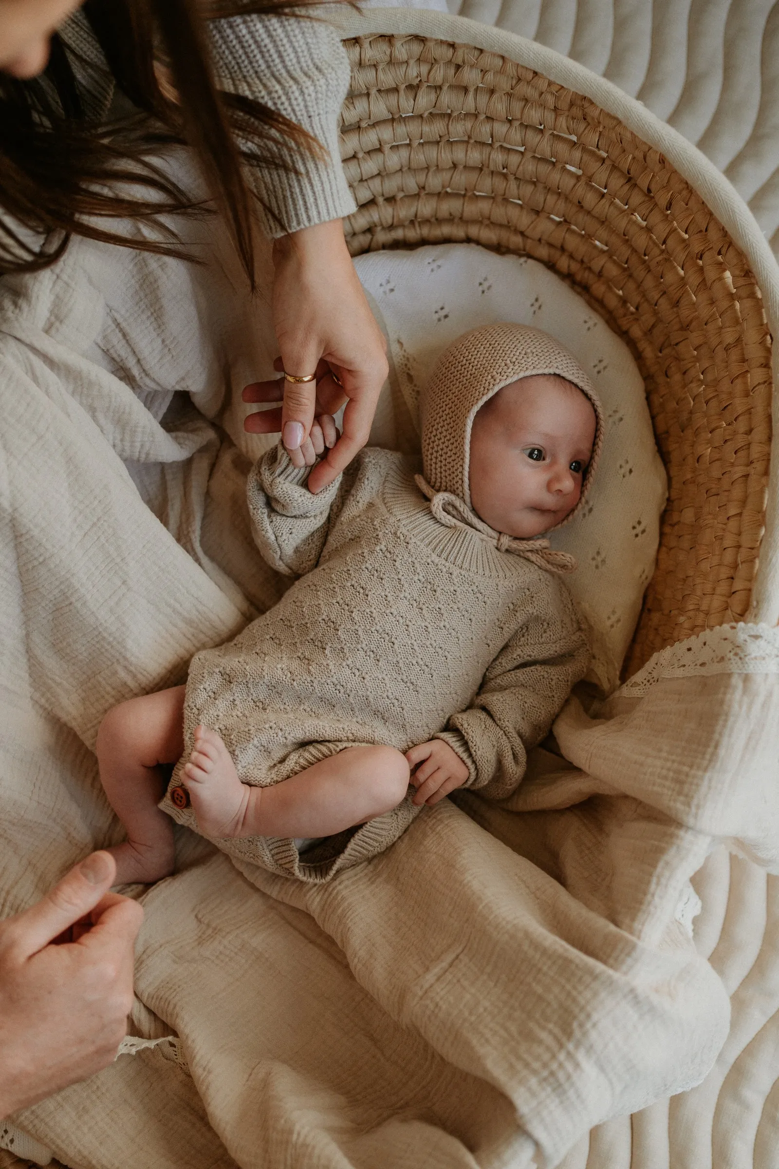 A big sister reaching towards her newborn sibling in a woven basket